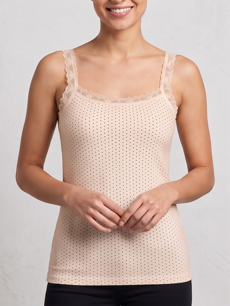 A woman wearing a light beige camisole tank top with a delicate lace-trimmed scoop neckline and a fine perforated dot pattern, paired with black pants against a light gray background.